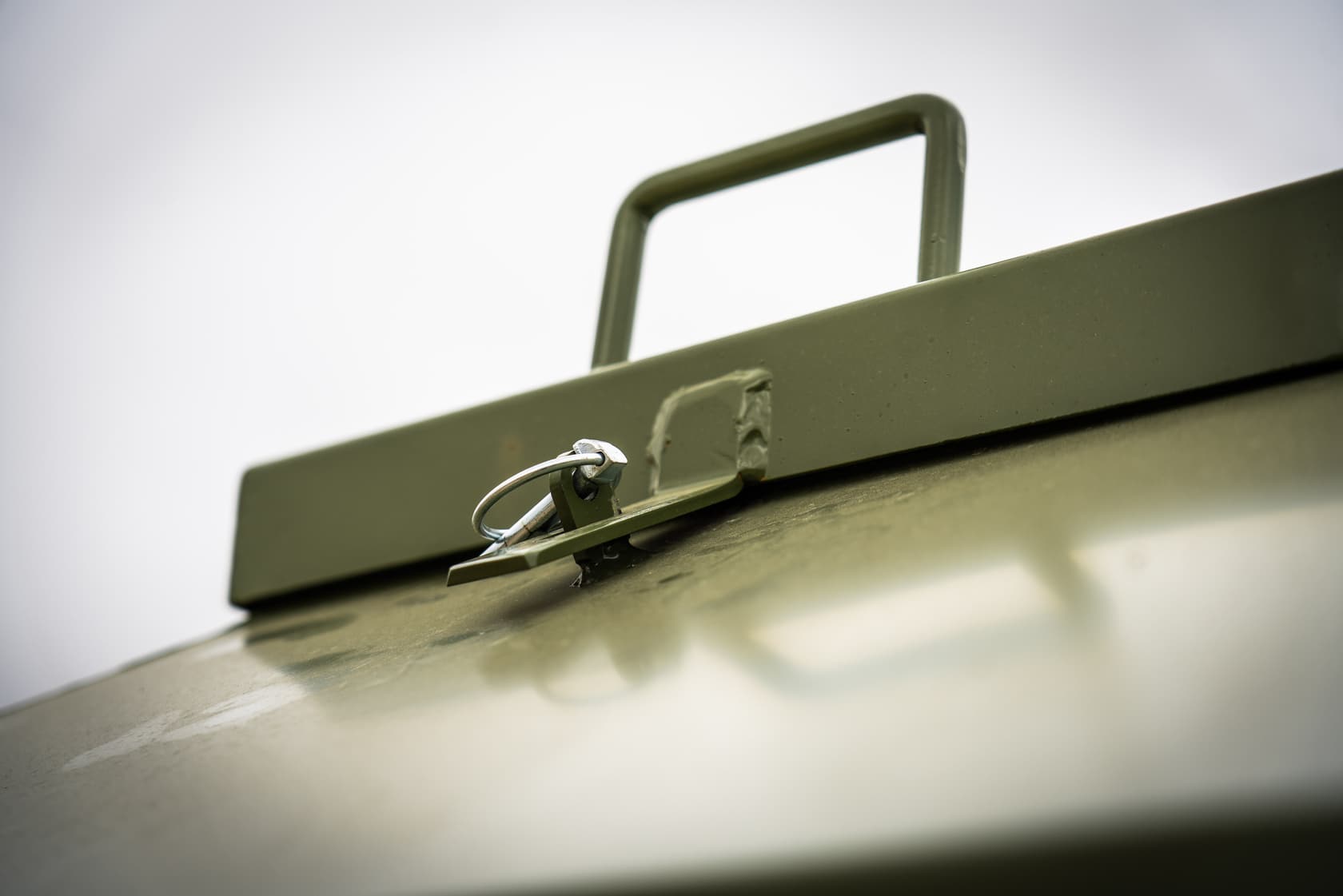 Close-up of the feeder lid: a bent-steel handle and a pinned latch, both powder-coated olive.