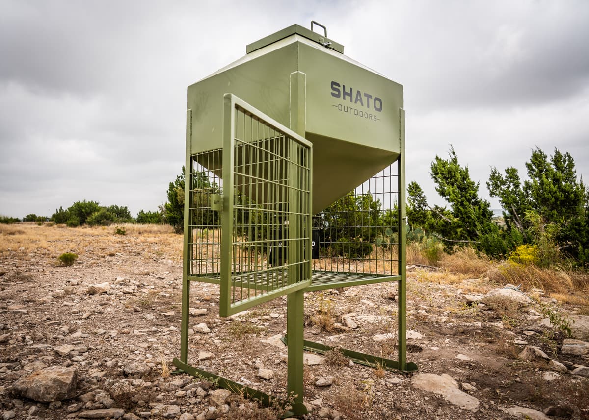 The feeder with its wire cage door swung open, showing the space under the hopper and the control box inside.