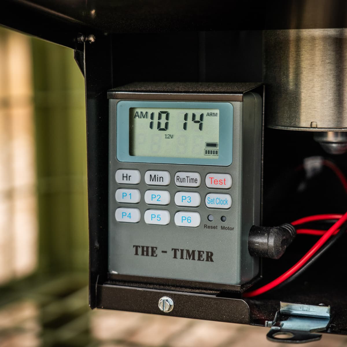 Close-up of the digital feeder timer, its display reading 10:14 AM above Hr, Min, Run Time, Test, Set Clock and program buttons.