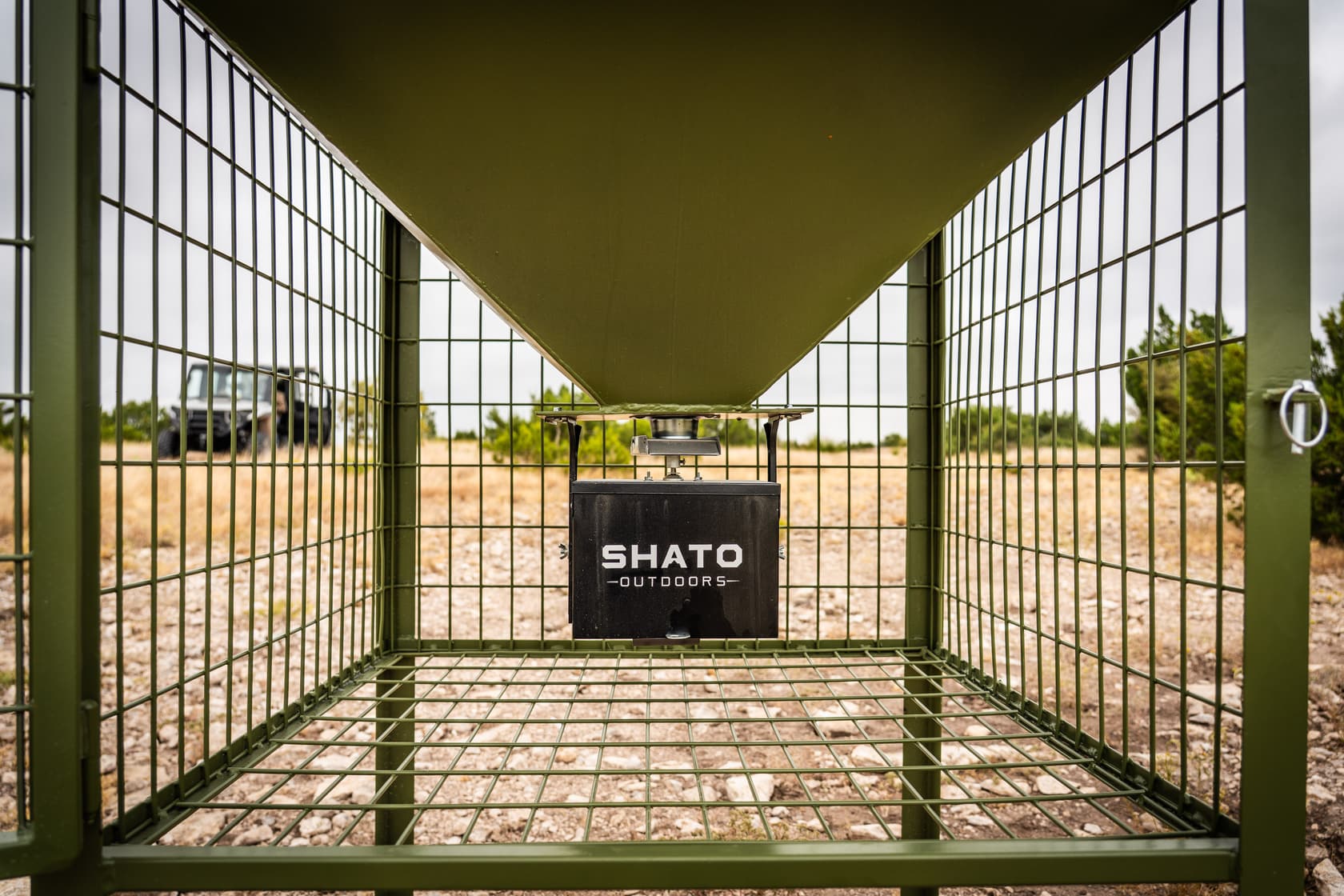 View straight through the wire cage: the hopper funnels down to the SHATO OUTDOORS control box hanging inside.