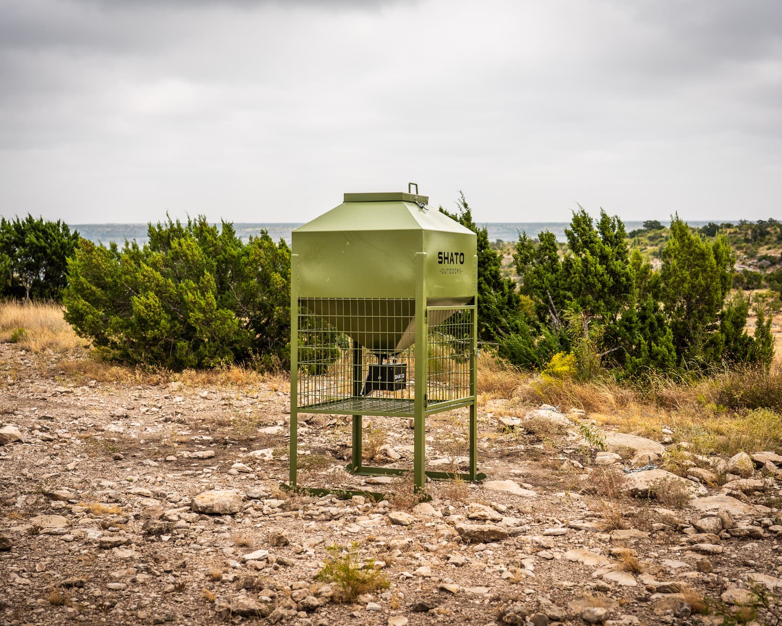 The feeder on an open caliche clearing ringed by cedar, with a long view across West Texas hills behind it.