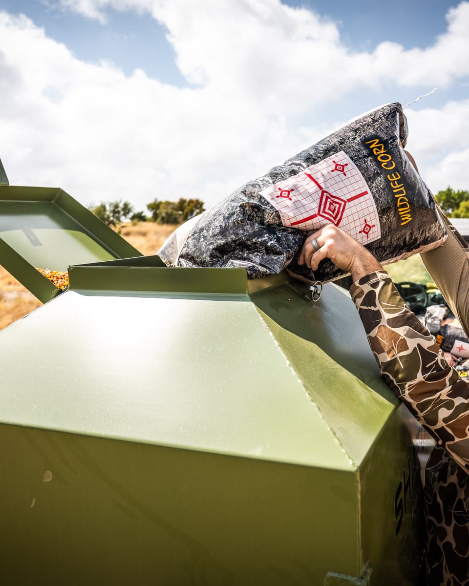 Pouring a bag of corn into the open lid at the top of the feeder.