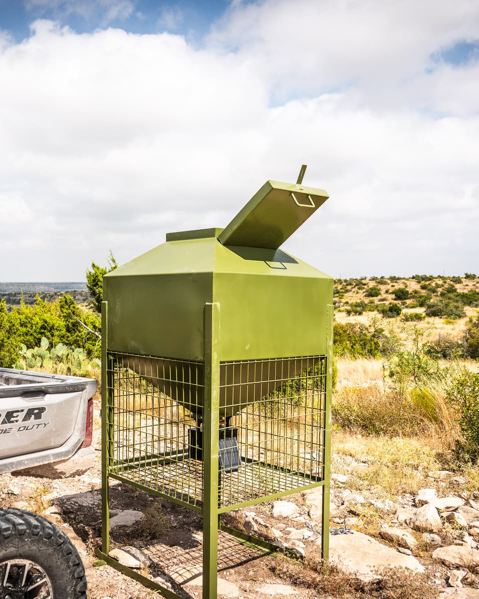 A utility vehicle loaded with feed bags parked beside the feeder, lid open, on a rise above West Texas brush country.