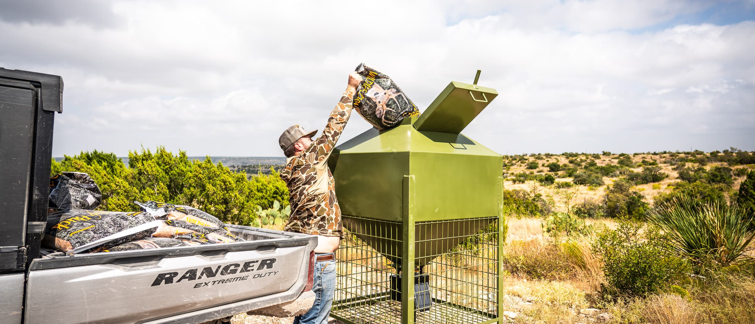 Reaching up from beside a utility vehicle to pour feed into the top of the feeder.